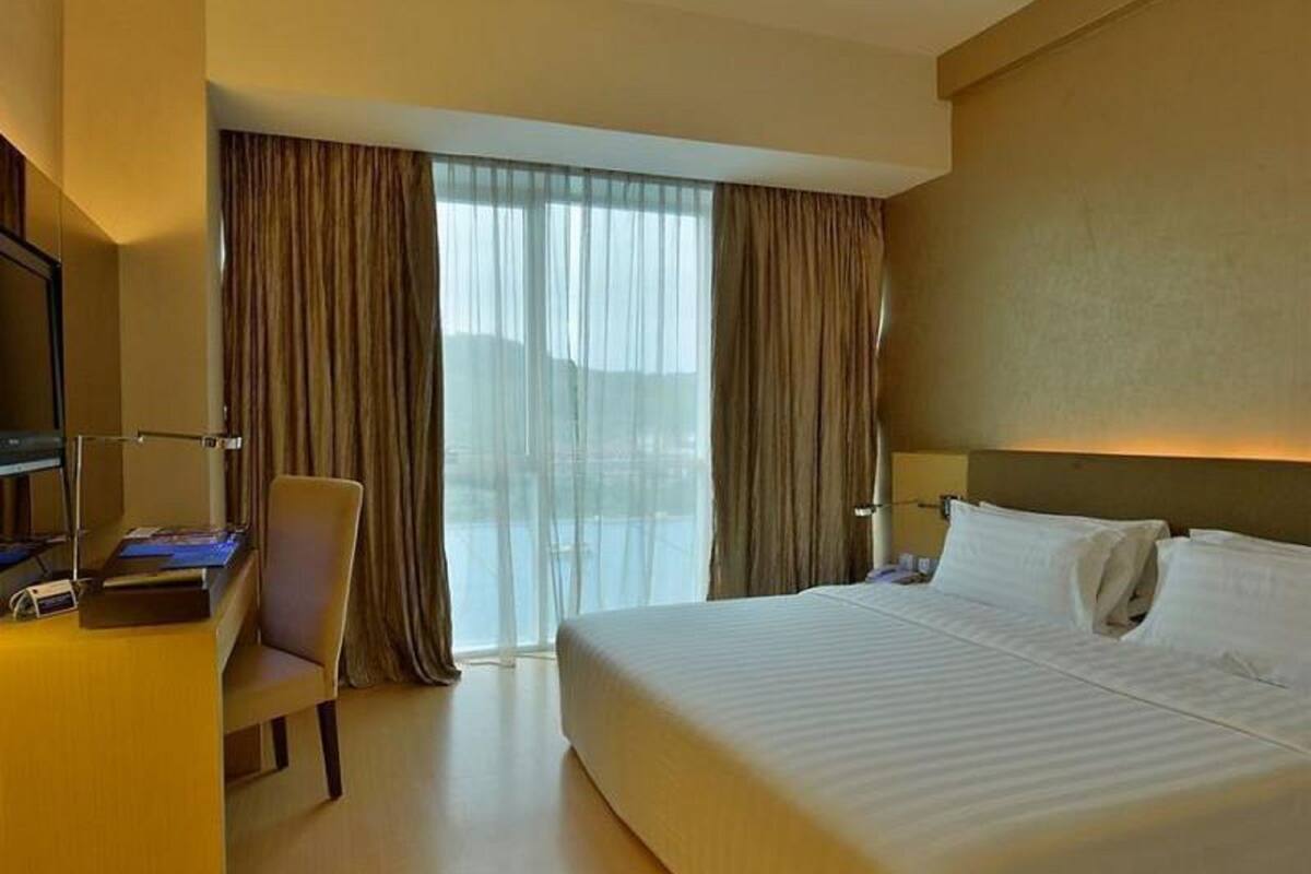 A hotel room with a bed, a desk, a chair, and a large window with curtains.