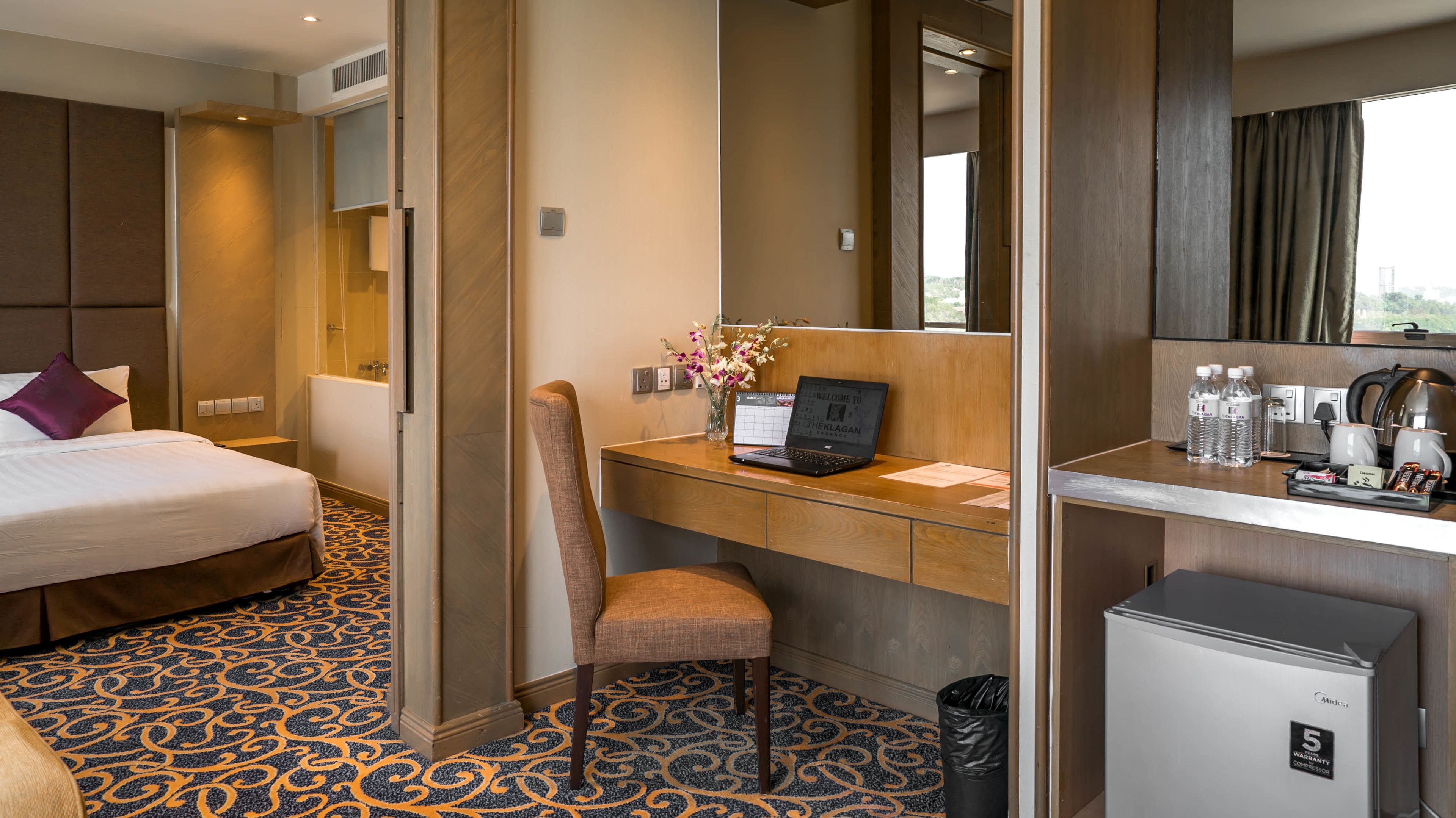 Een hotelkamer met een bed, bureau, stoel en een kleine koelkast.