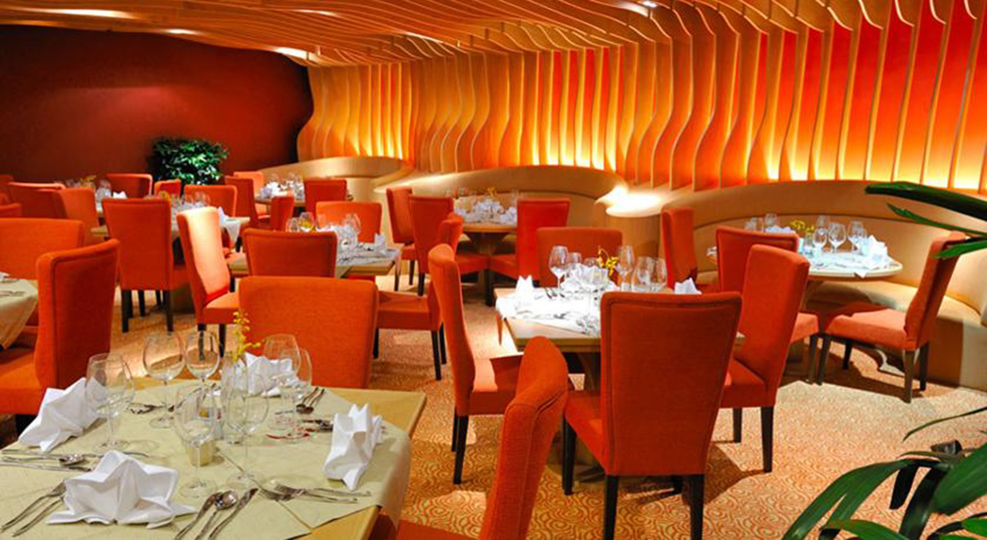 A restaurant with orange chairs and tables, each set with cutlery and glasses.