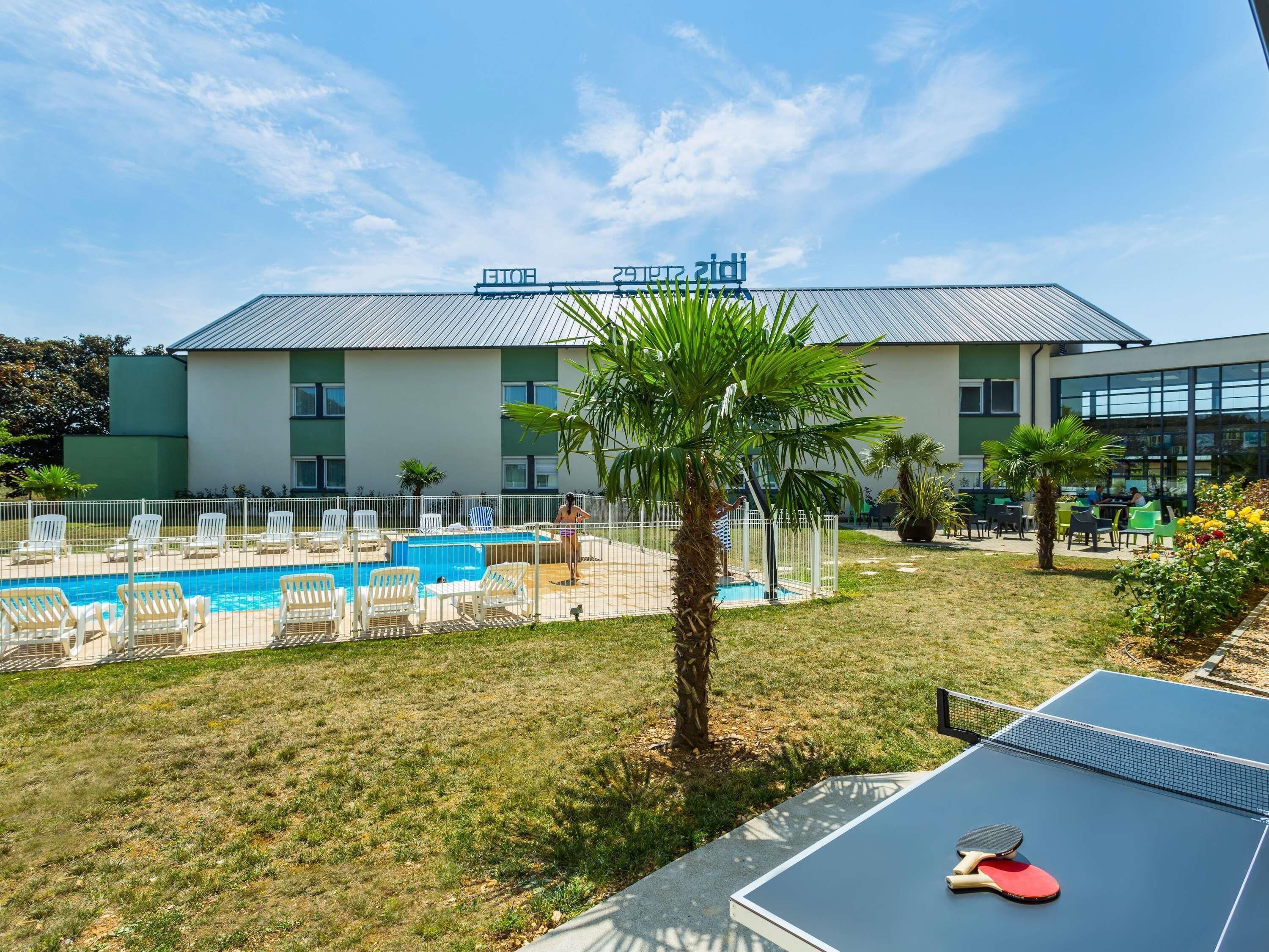 A hotel with a swimming pool, outdoor seating, and a tennis court.