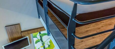 A bunk bed with a white mattress and pillows, a wooden floor, a wall-mounted TV, and a floral wall decoration.
