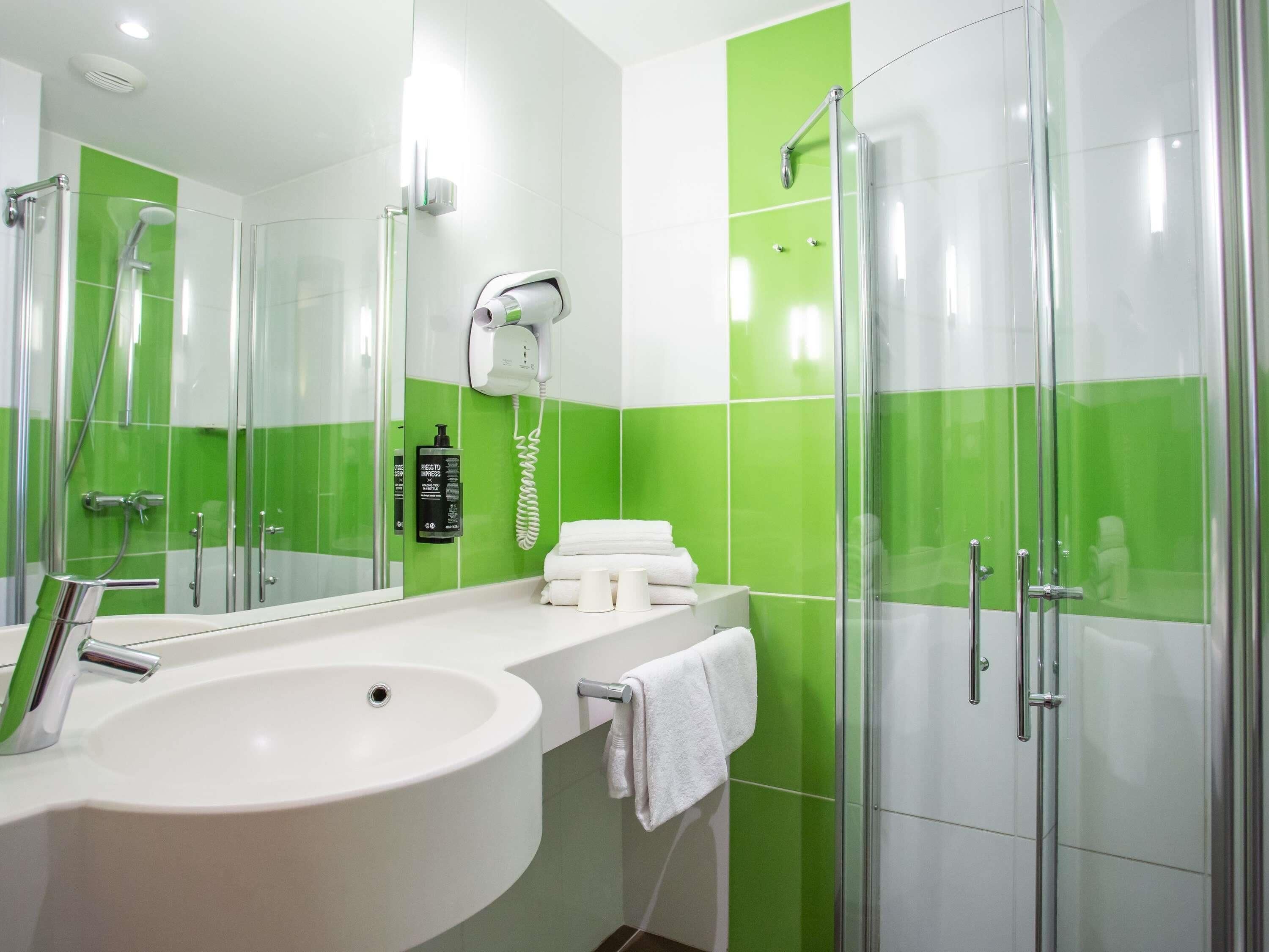 A modern bathroom with a large sink, a glass shower enclosure, and green-tiled walls.
