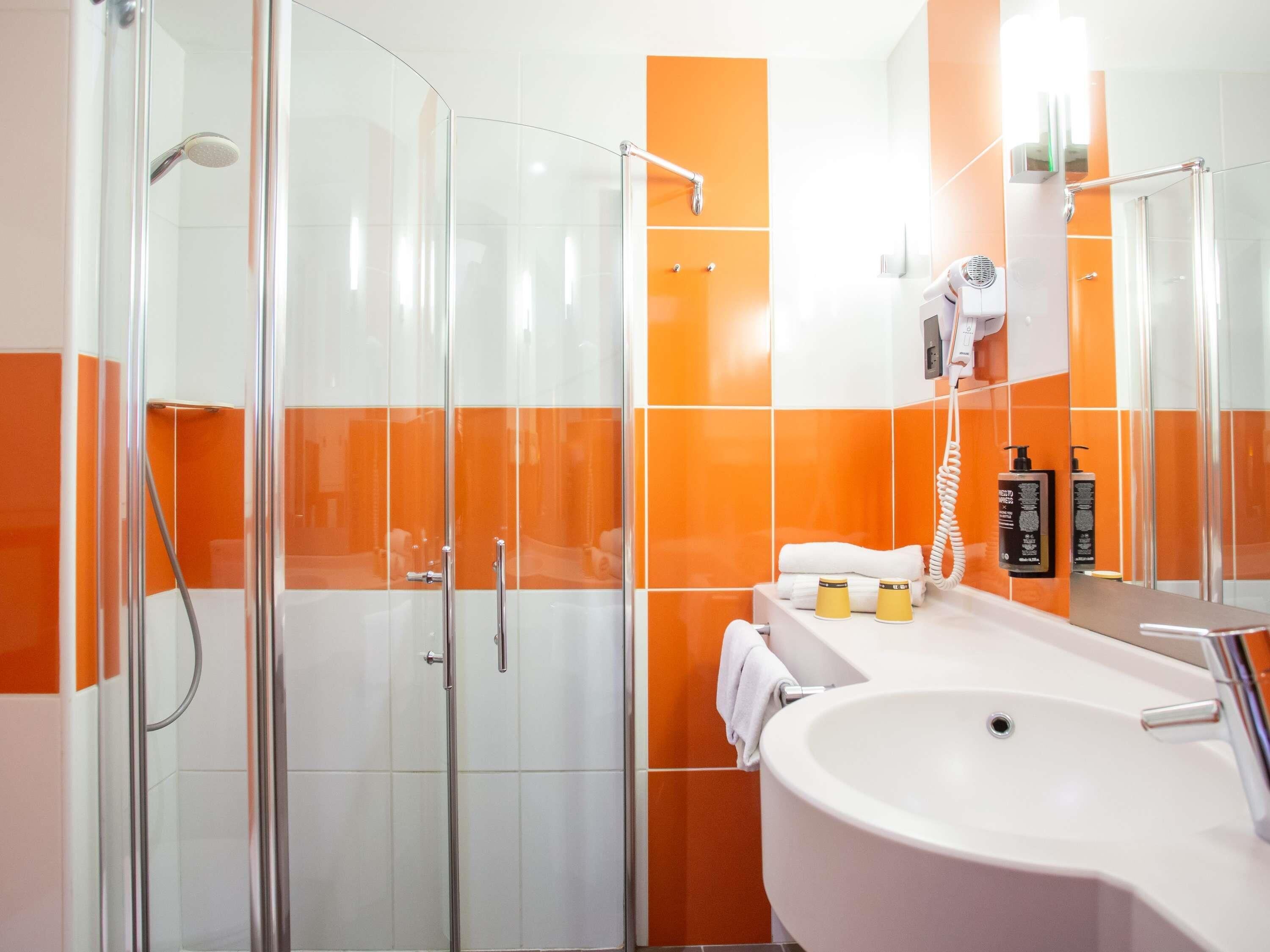 Un baño moderno con cabina de ducha de vidrio, lavabo blanco y paredes cubiertas de azulejos naranjas.