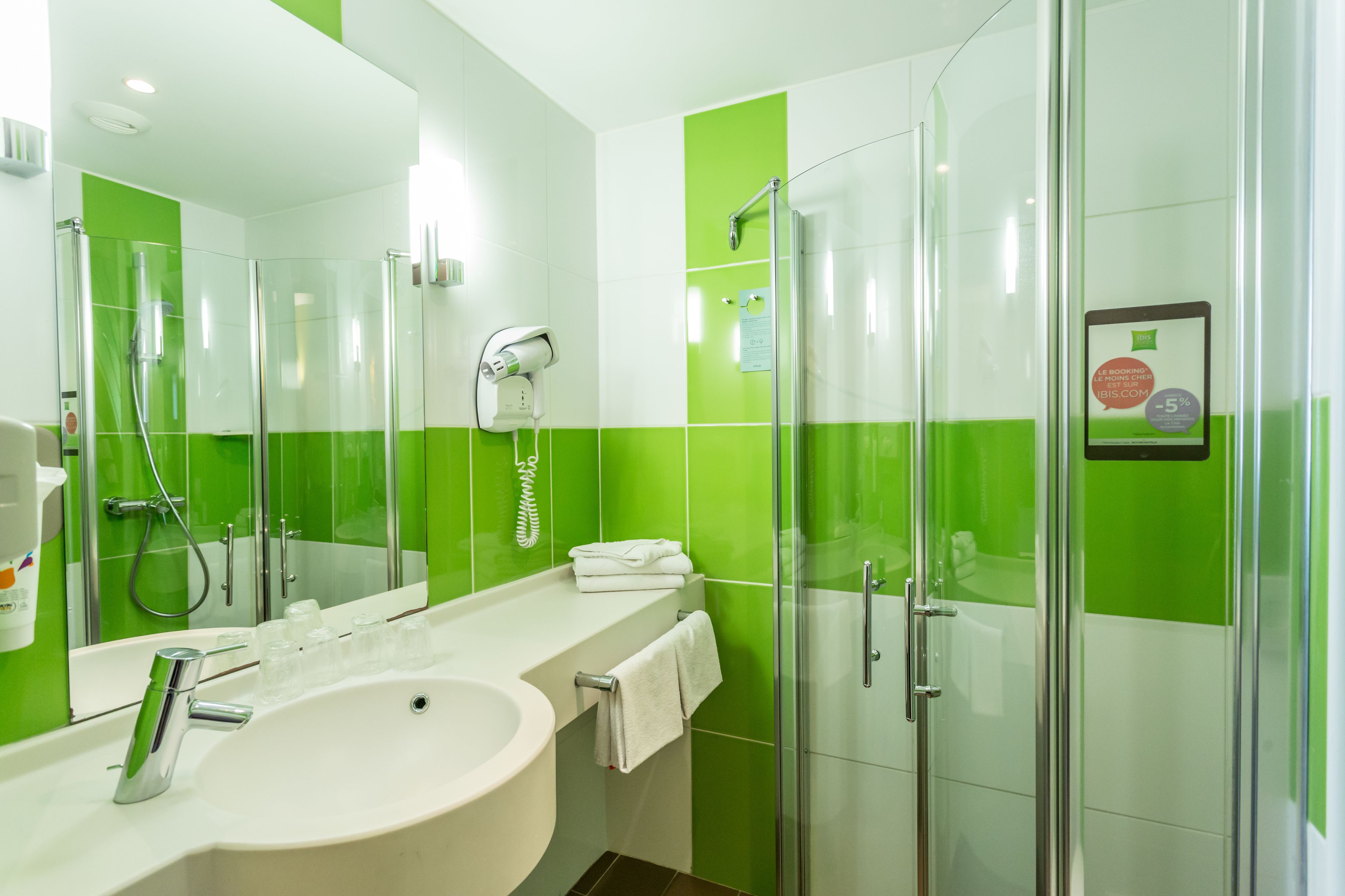 Un baño moderno con cabina de ducha de vidrio, un lavabo blanco y una pared con azulejos verdes.