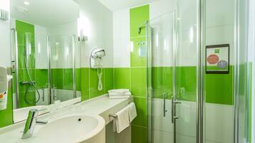 Un baño moderno con cabina de ducha de vidrio, un lavabo blanco y una pared con azulejos verdes.