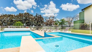 A swimming pool with multiple lanes, surrounded by a white fence, and a green building in the background. - ibis Styles Bourges (Bourges)