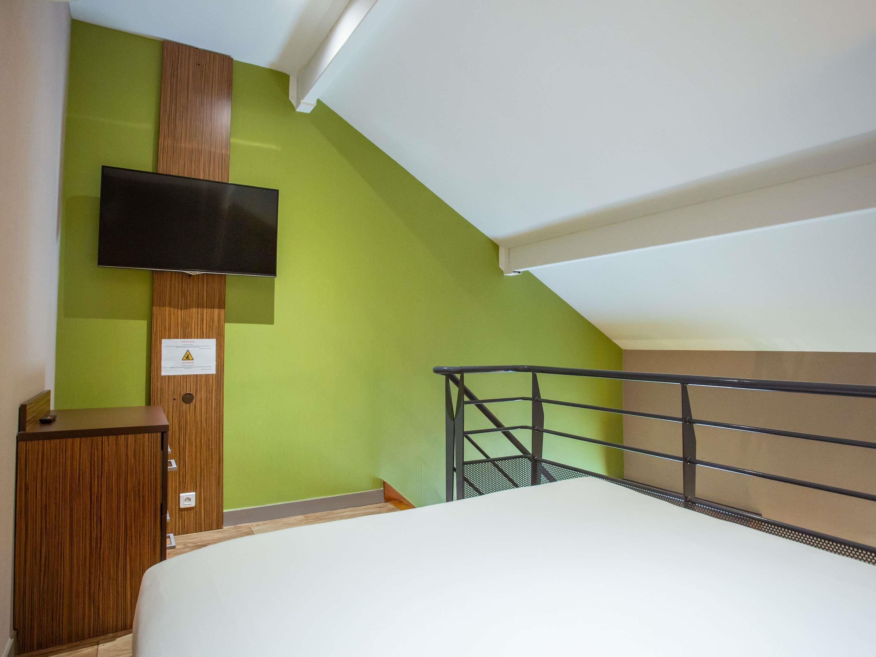 A room with a bed, a desk, a television mounted on a wall, and a staircase.
