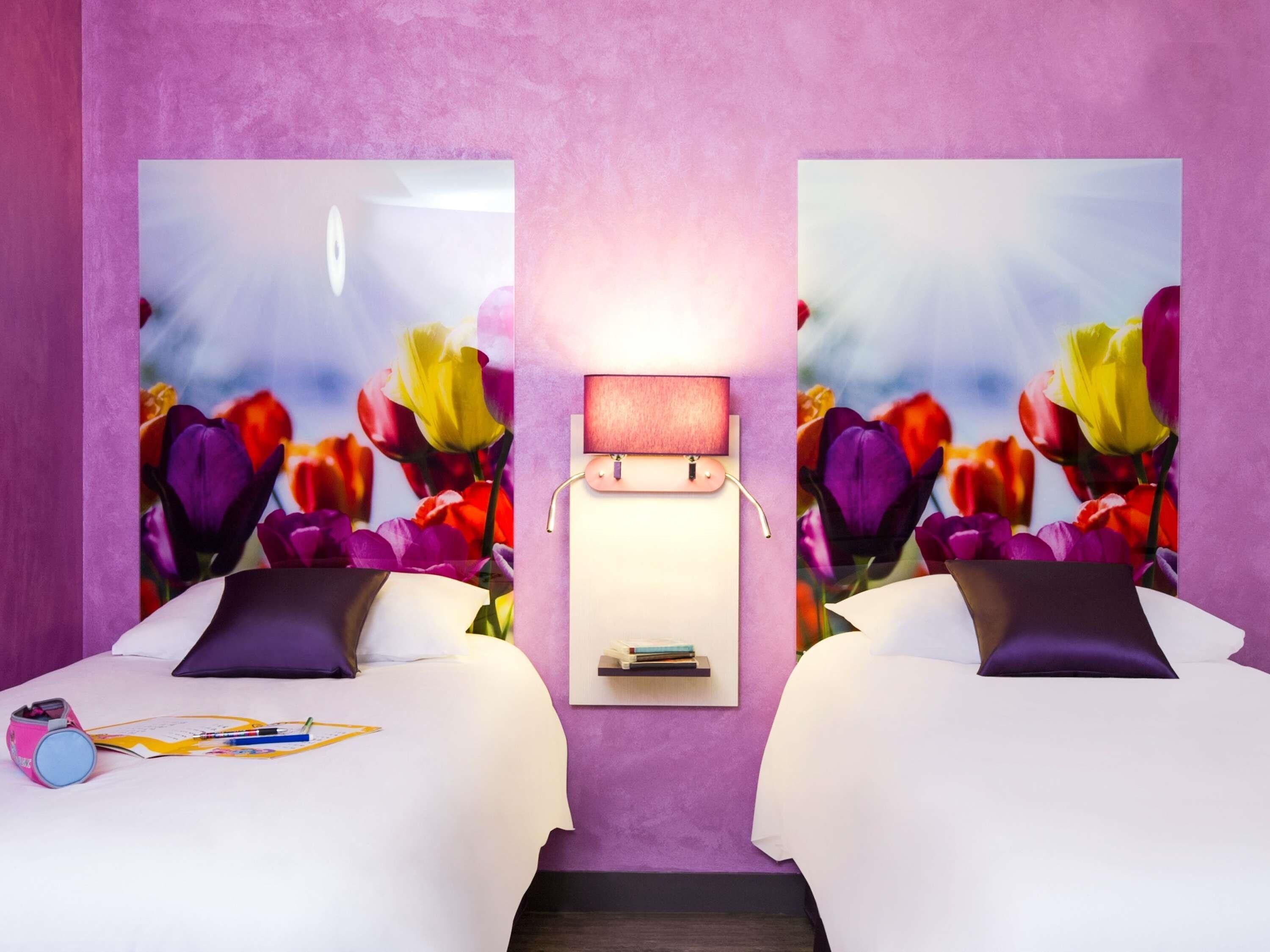 Una habitación de hotel con dos camas, una mesita de noche con lámpara y un estante en la pared.