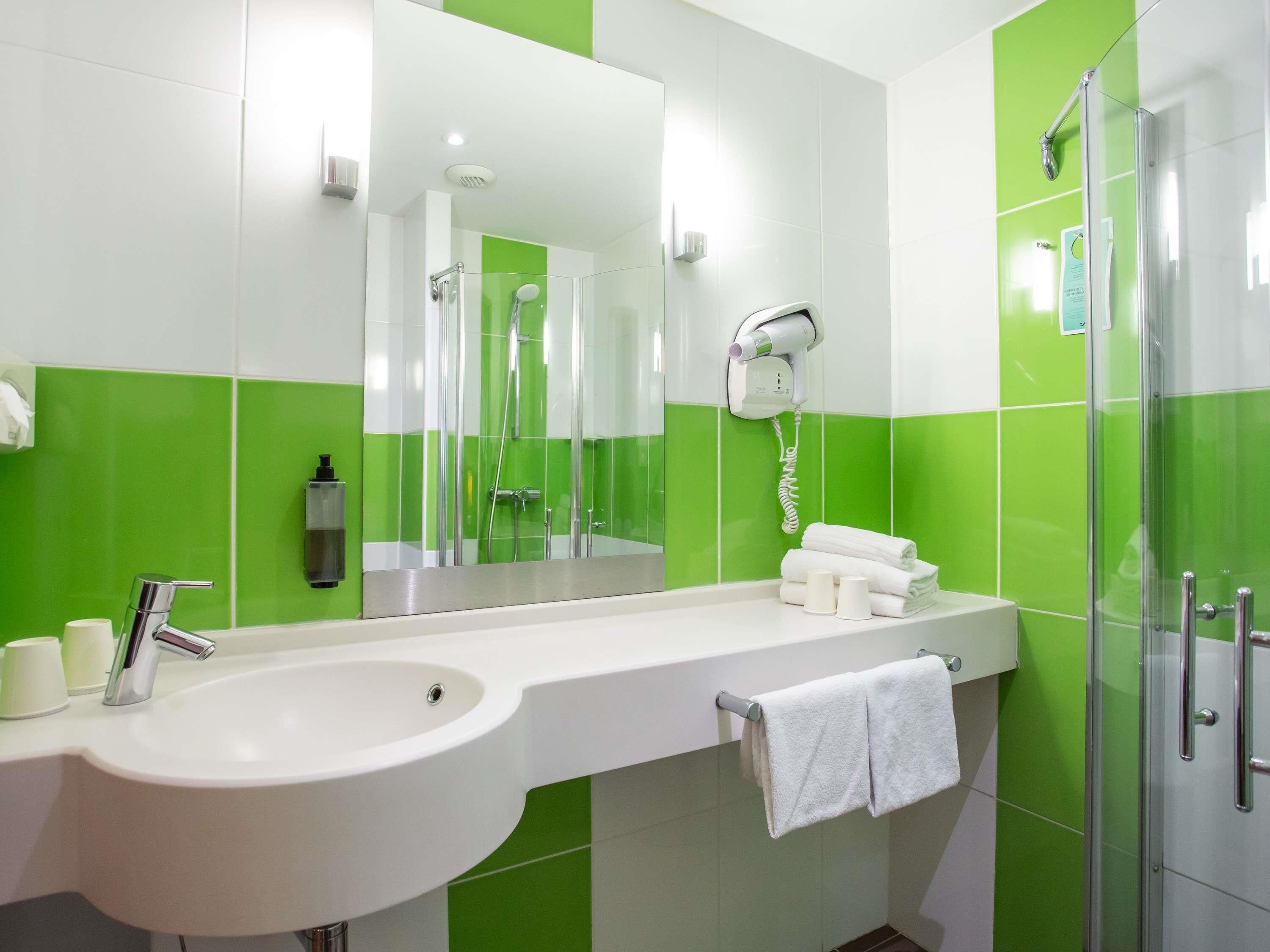 A bathroom with a white sink, a glass shower enclosure, and green tiles.