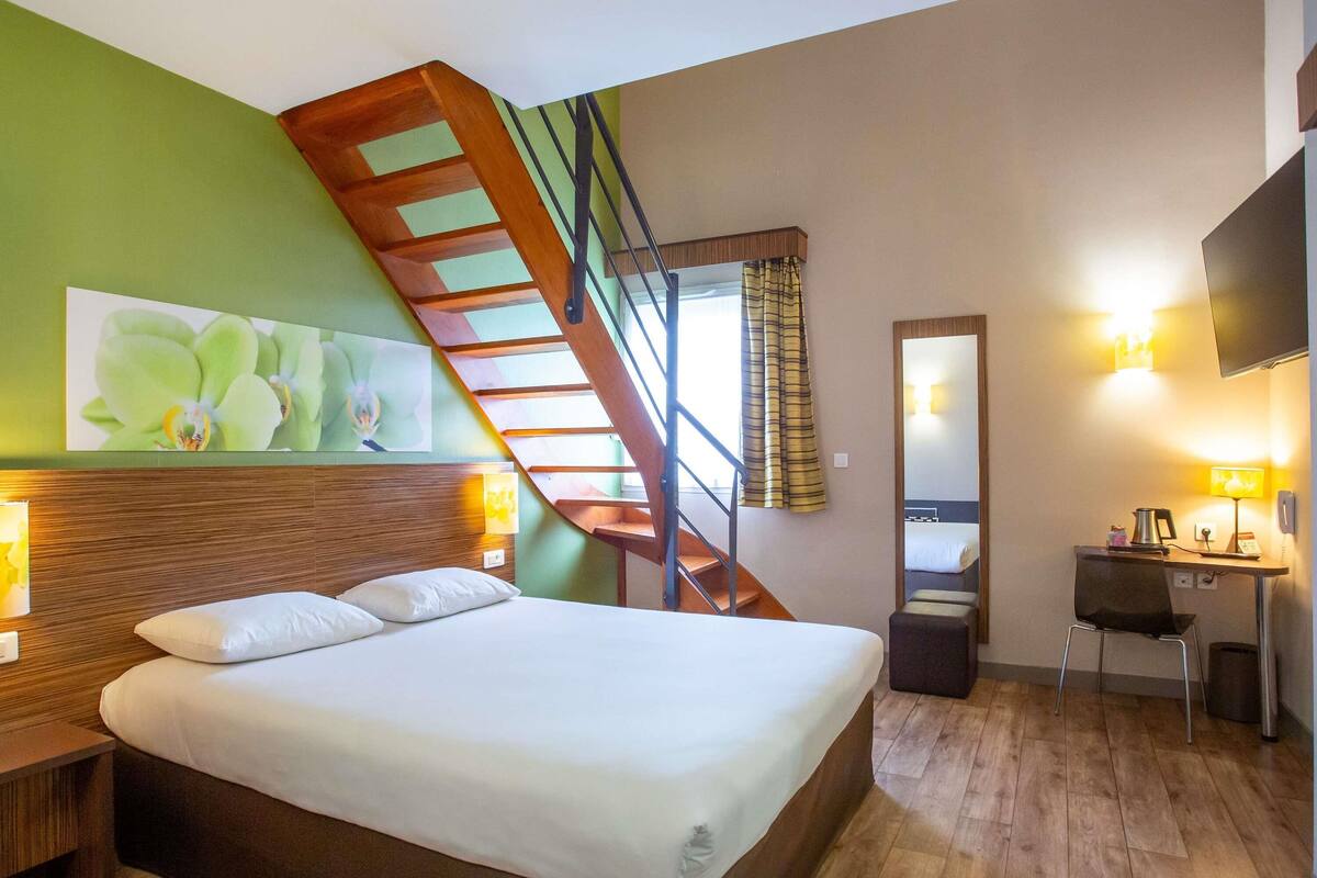 A hotel room with a bed, a desk, a chair, a mirror, a staircase, and a TV.