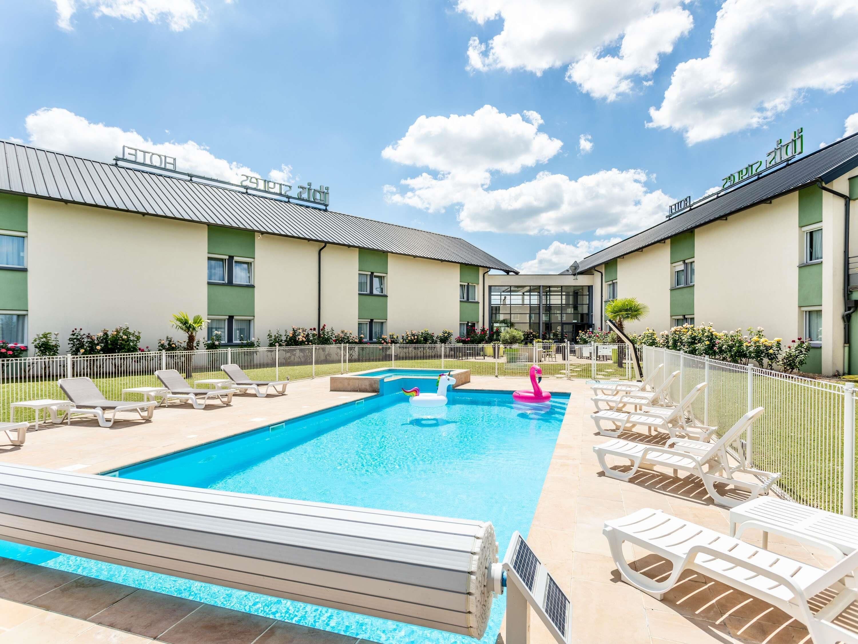 A hotel with a swimming pool, lounge chairs, and a fenced garden area.