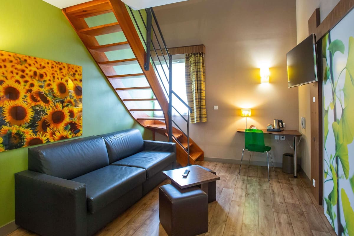 A modern living room with a black leather sofa, a wooden staircase, a green wall, and a painting of sunflowers.