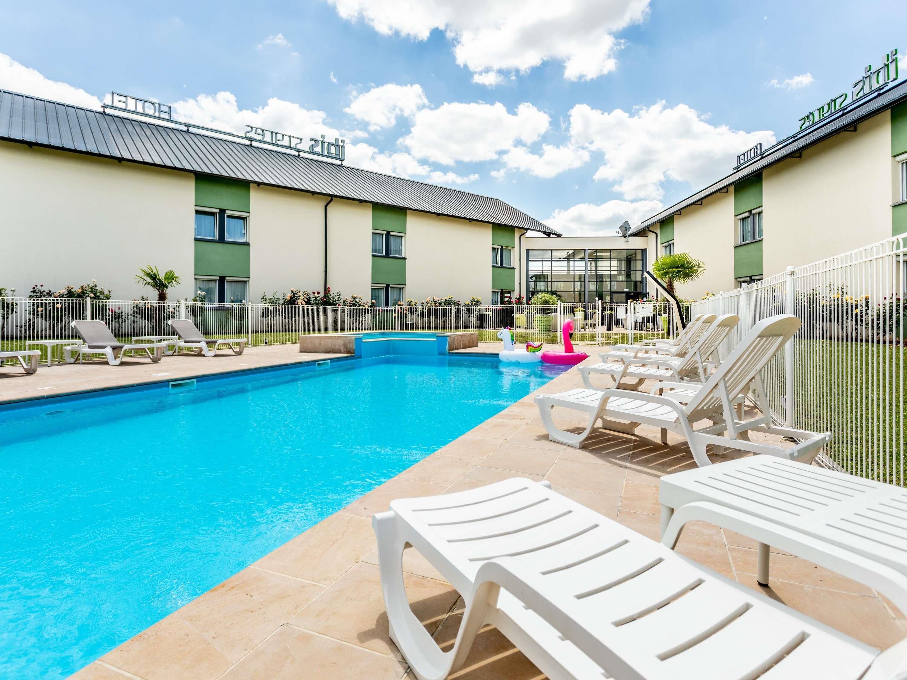 A swimming pool with lounge chairs, a fenced area, and a building with a green facade.