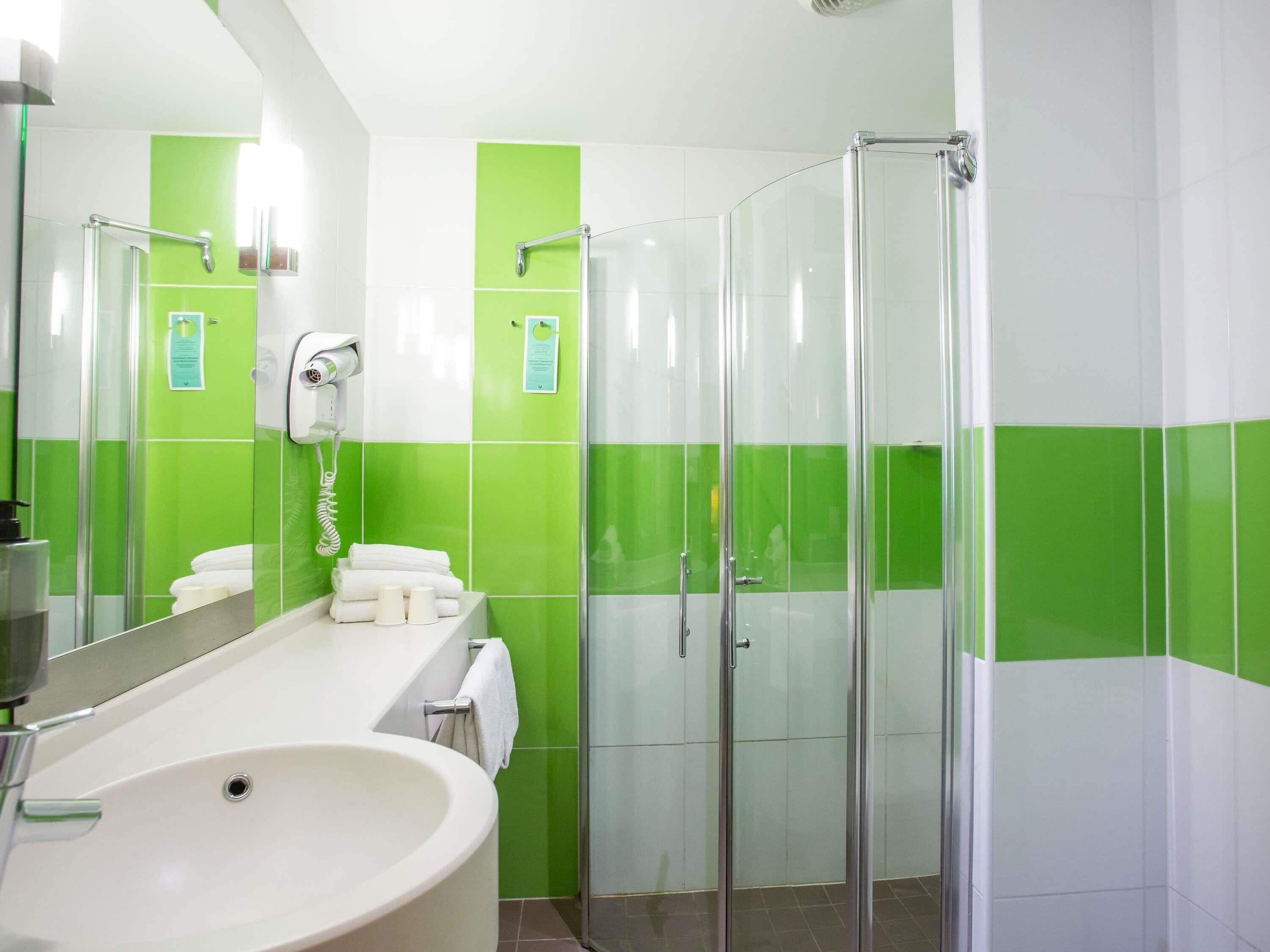Un baño moderno con un lavamanos grande, cabina de ducha de cristal y azulejos verdes y blancos.