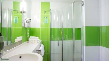 A modern bathroom with a large sink, a glass shower enclosure, and green and white tiles.