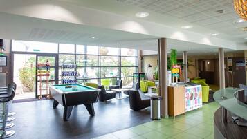 A pool table in a brightly lit indoor area with large windows, green and black chairs, and a reception desk.