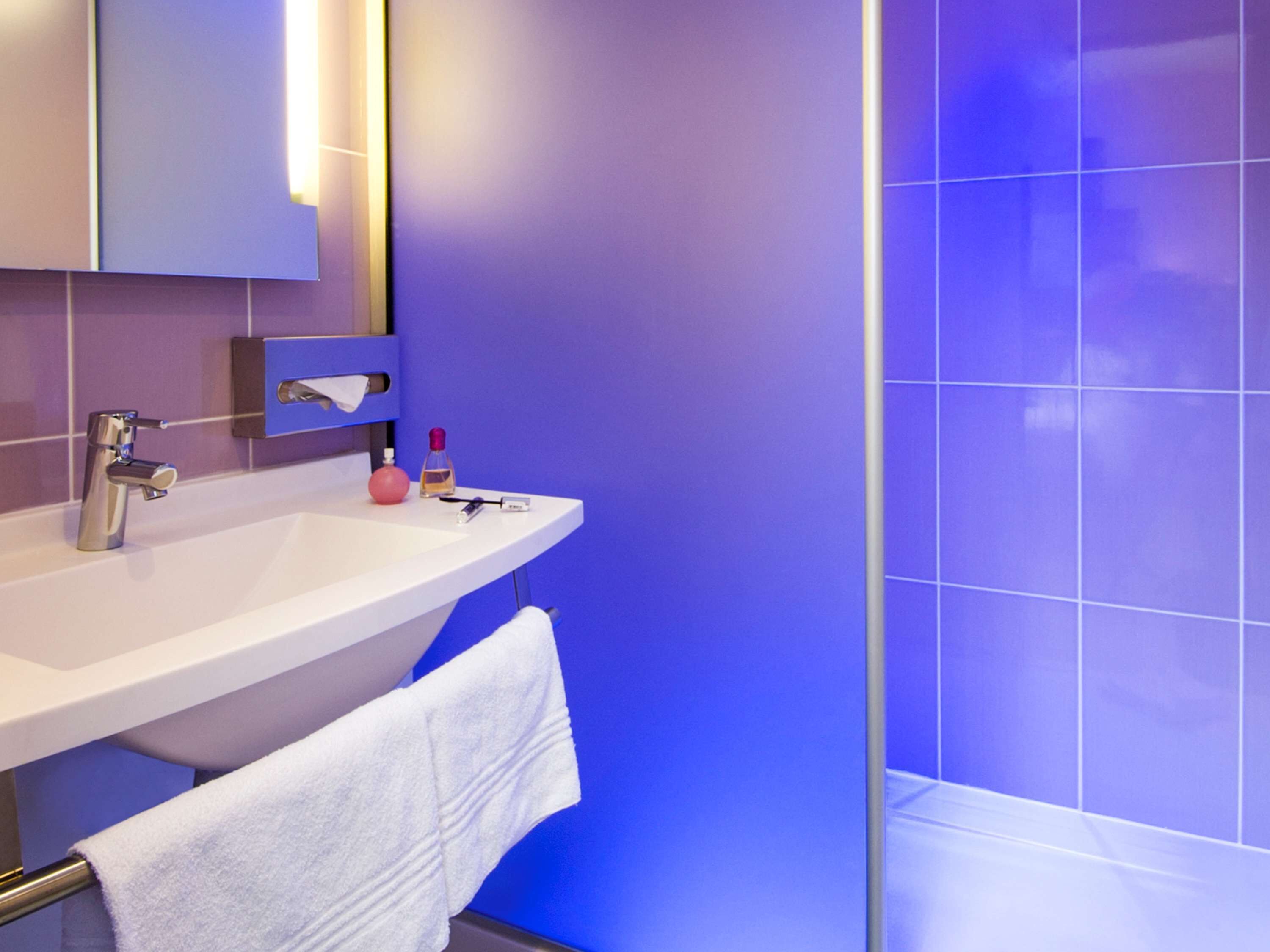 Un baño moderno con un lavamanos blanco, un espejo y una ducha con paredes de azulejos azules.