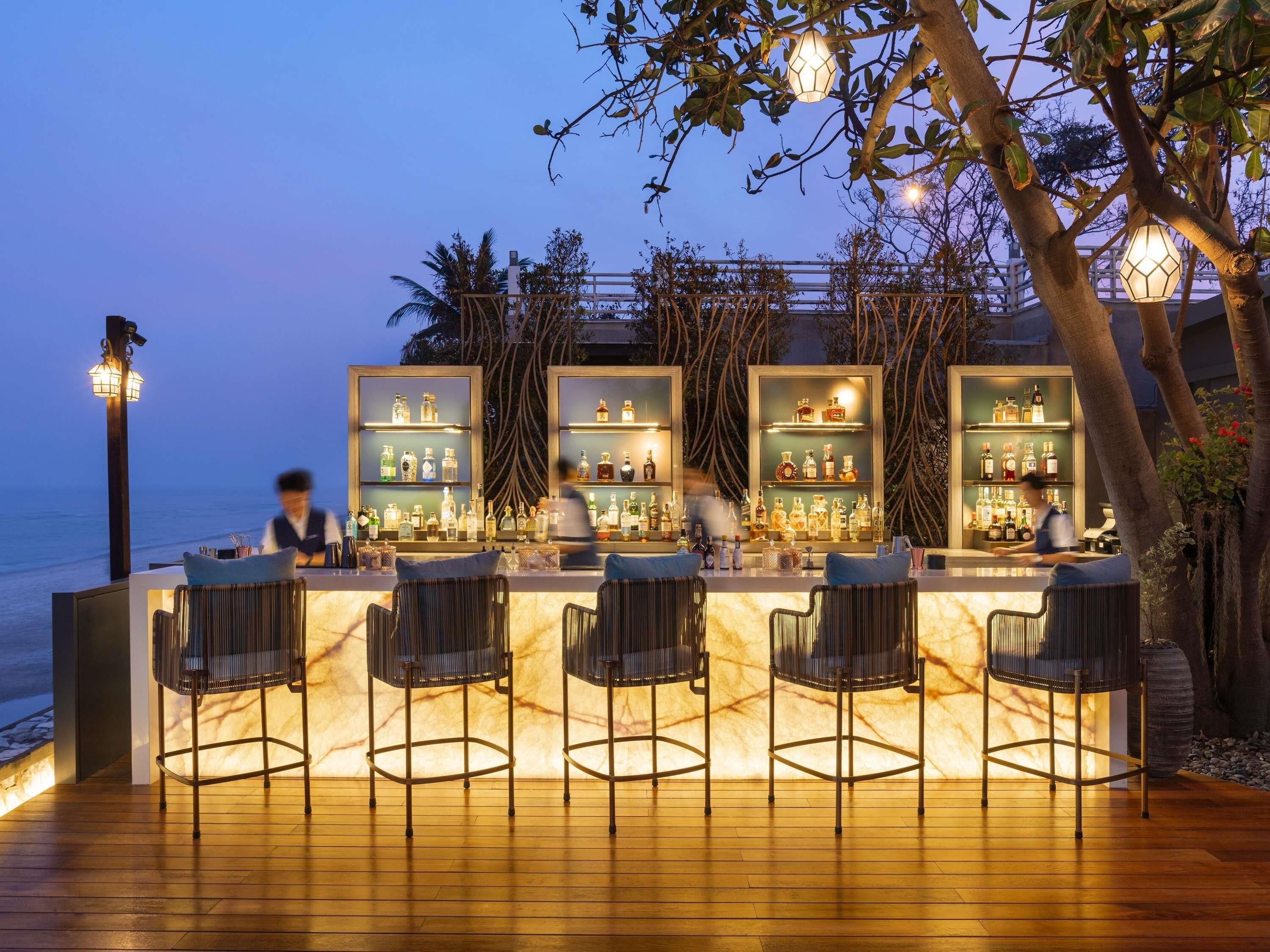 Um bar com piso de madeira, banquetas e prateleiras cheias de garrafas de bebidas.