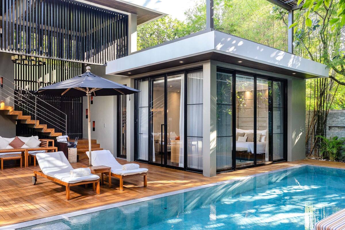 A modern house with a swimming pool, wooden deck, and a glass-enclosed bedroom.