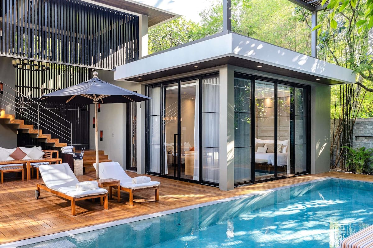 A modern house with a swimming pool, wooden deck, and a glass-enclosed bedroom.
