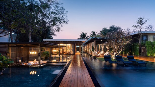 A modern resort with a wooden deck, a swimming pool, and lounge chairs.