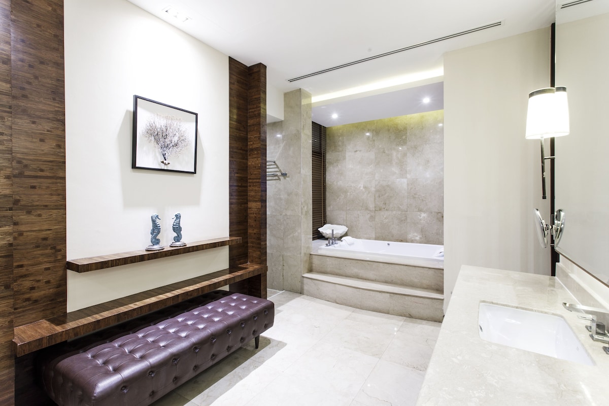 A modern bathroom with a marble sink, a bench, a bathtub, and a framed artwork on the wall.