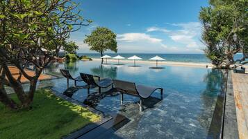 An infinity pool with clear water, surrounded by lounge chairs and umbrellas, overlooking a beach.