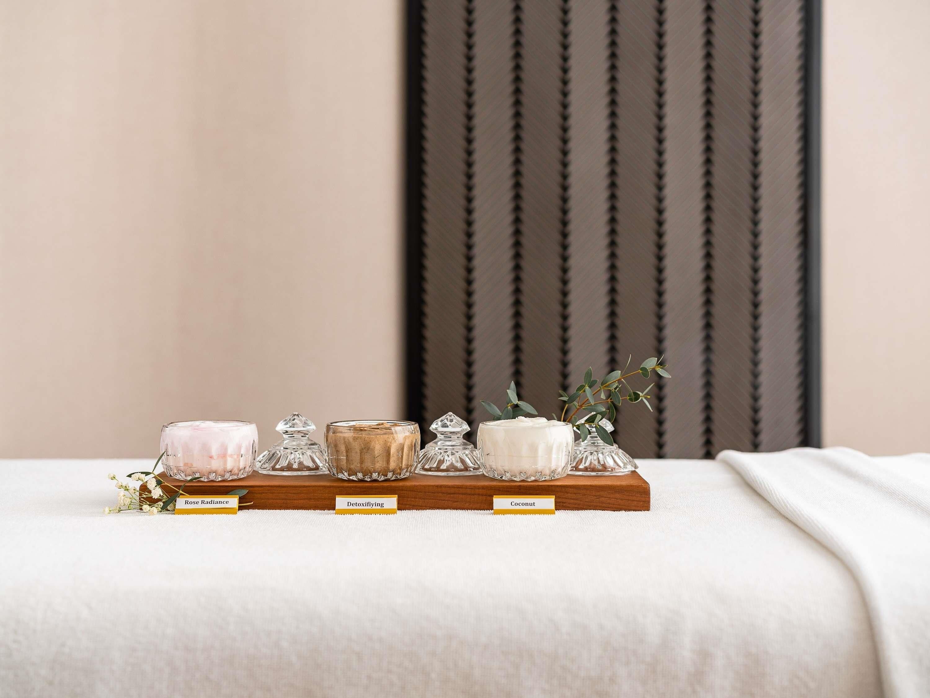 A wooden shelf with glass containers labeled 'Rose Radiance,' 'Detoxifying,' and 'Coconut.'
