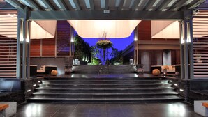 A modern hotel lobby with a central staircase, seating areas, and a decorative plant arrangement.