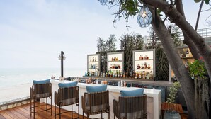 A bar with a view of the ocean, wicker chairs, and a large vase with plants.