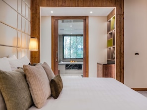 Una camera da letto con un letto grande, una testiera in legno, un comodino con una lampada, e vista sul bagno e su una finestra.