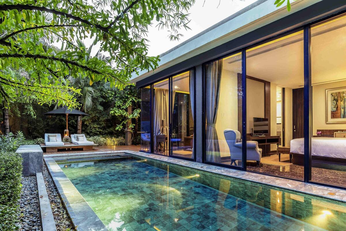 A modern hotel room with a glass wall, a pool, and a seating area with lounge chairs.