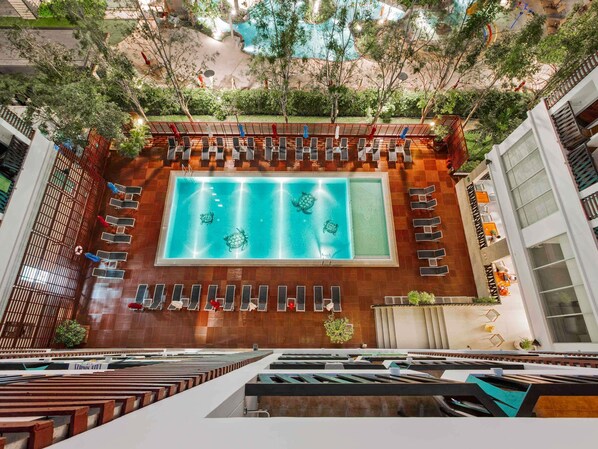 A rooftop swimming pool with multiple levels of seating and a view of the surrounding greenery.