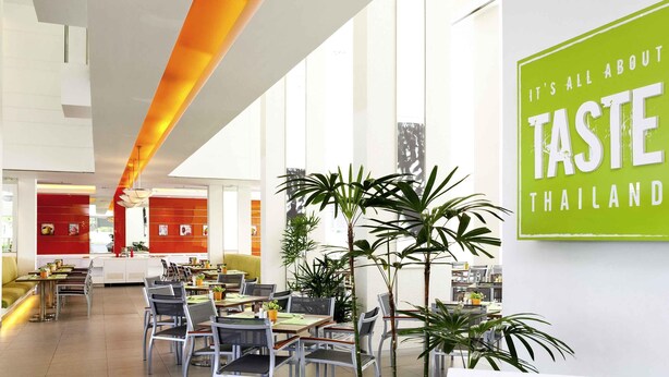 A modern restaurant interior with high ceilings, large windows, and a prominent green sign. - ibis Pattaya (Pattaya)