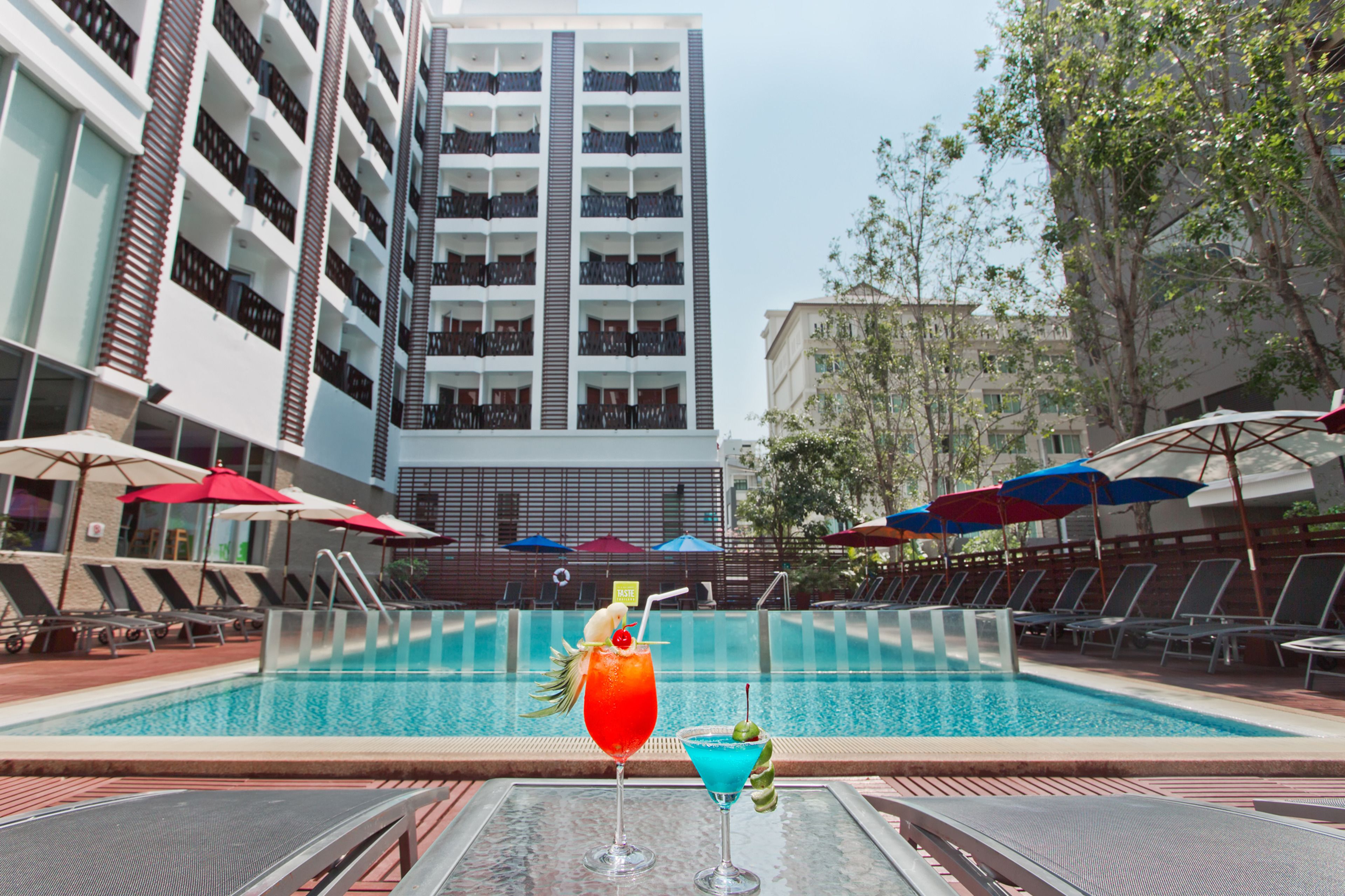Una piscina con sillas de descanso y sombrillas, rodeada por un edificio alto.