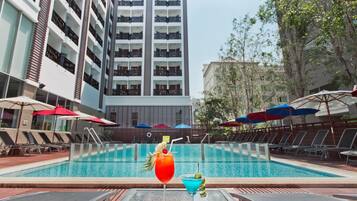 Una piscina con sillas de descanso y sombrillas, rodeada por un edificio alto.