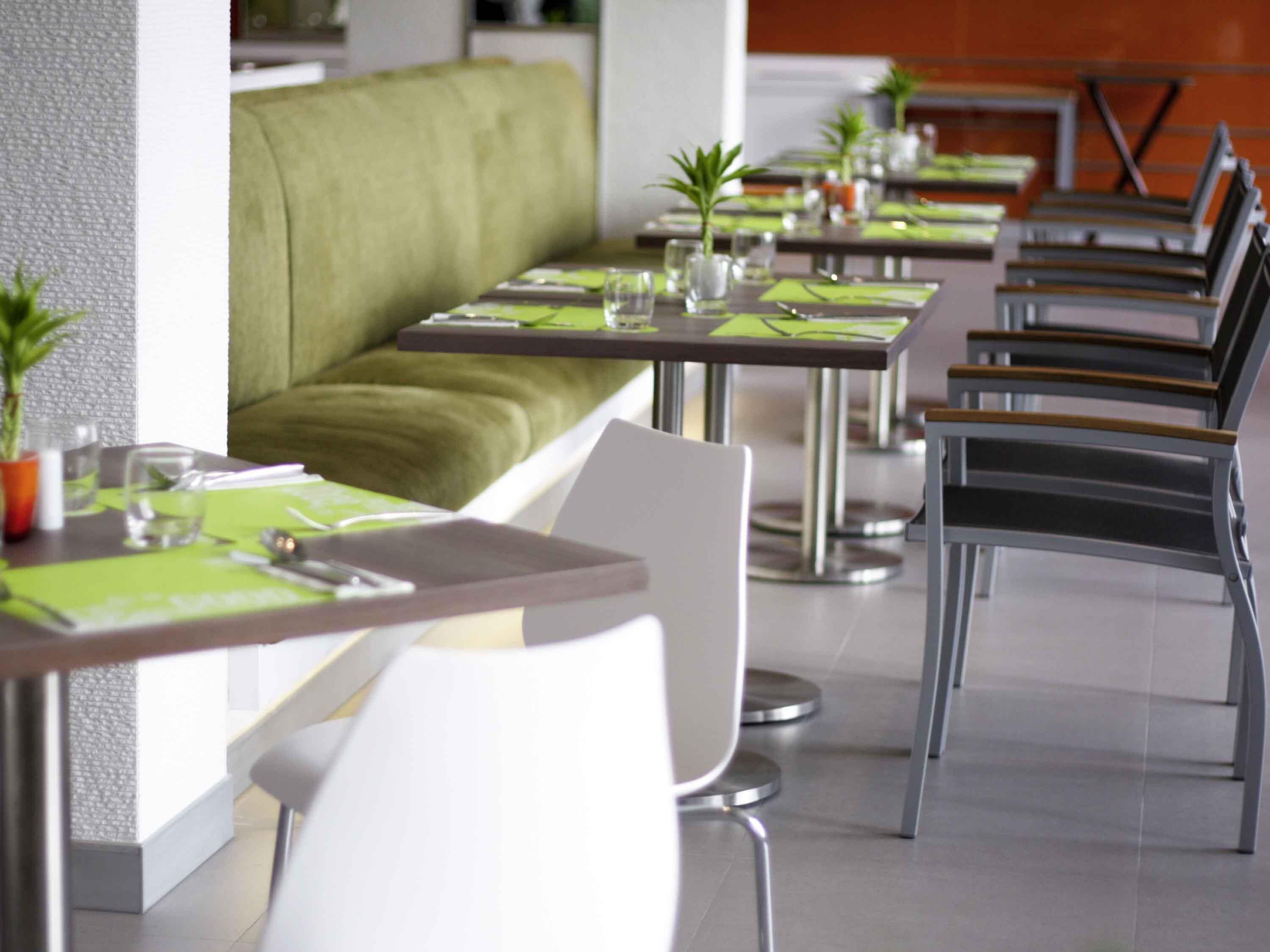 A modern dining area with green cushioned seating, white chairs, and metal tables.