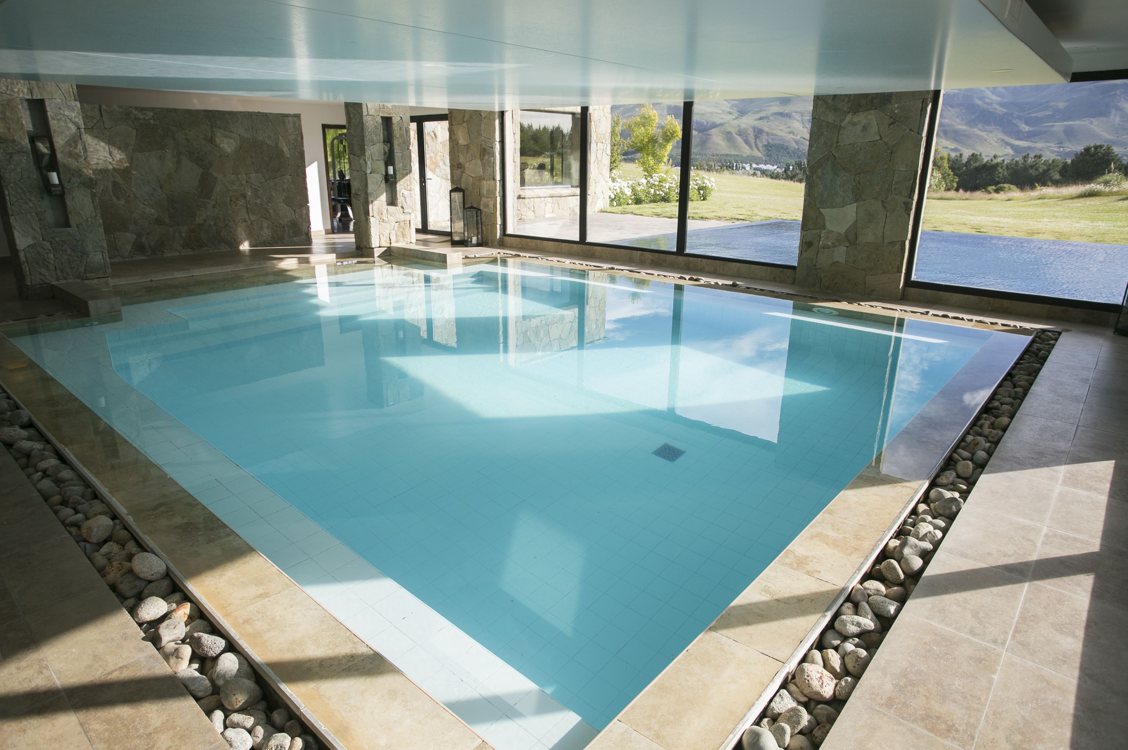 Una amplia piscina interior con paredes de piedra y vistas a un lago y montañas.
