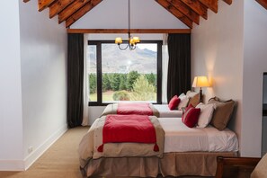 Une chambre avec deux lits, une grande fenêtre donnant sur les montagnes et un lustre.