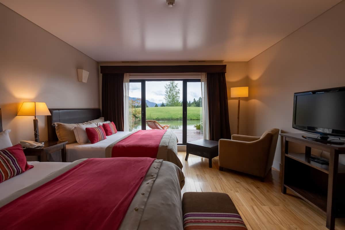 Ein Hotelzimmer mit zwei Betten, einem Fernseher, einem Schreibtisch und Blick auf einen See und Berge.