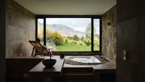 Ein modernes Badezimmer mit großem Fenster, einer Badewanne, einem Holzstuhl und einer Schale.