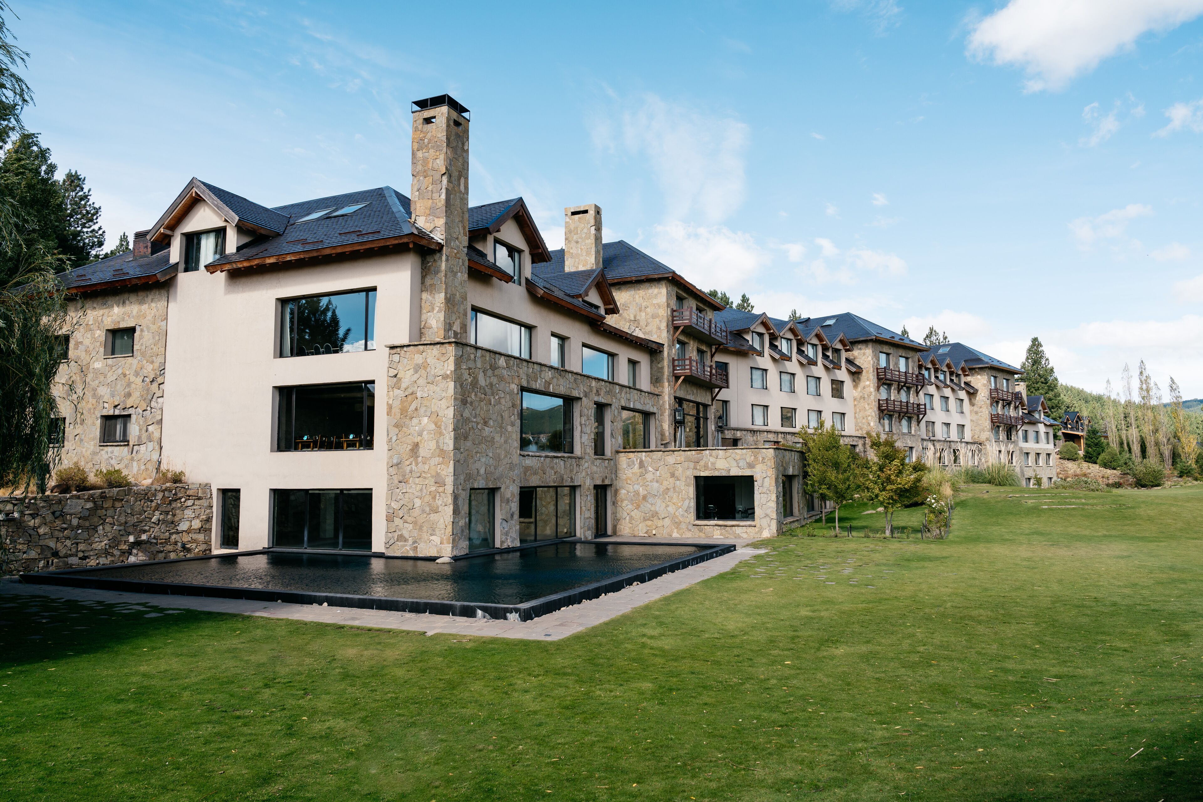 A modern multi-story building with stone and wood exterior, large windows, and a swimming pool.
