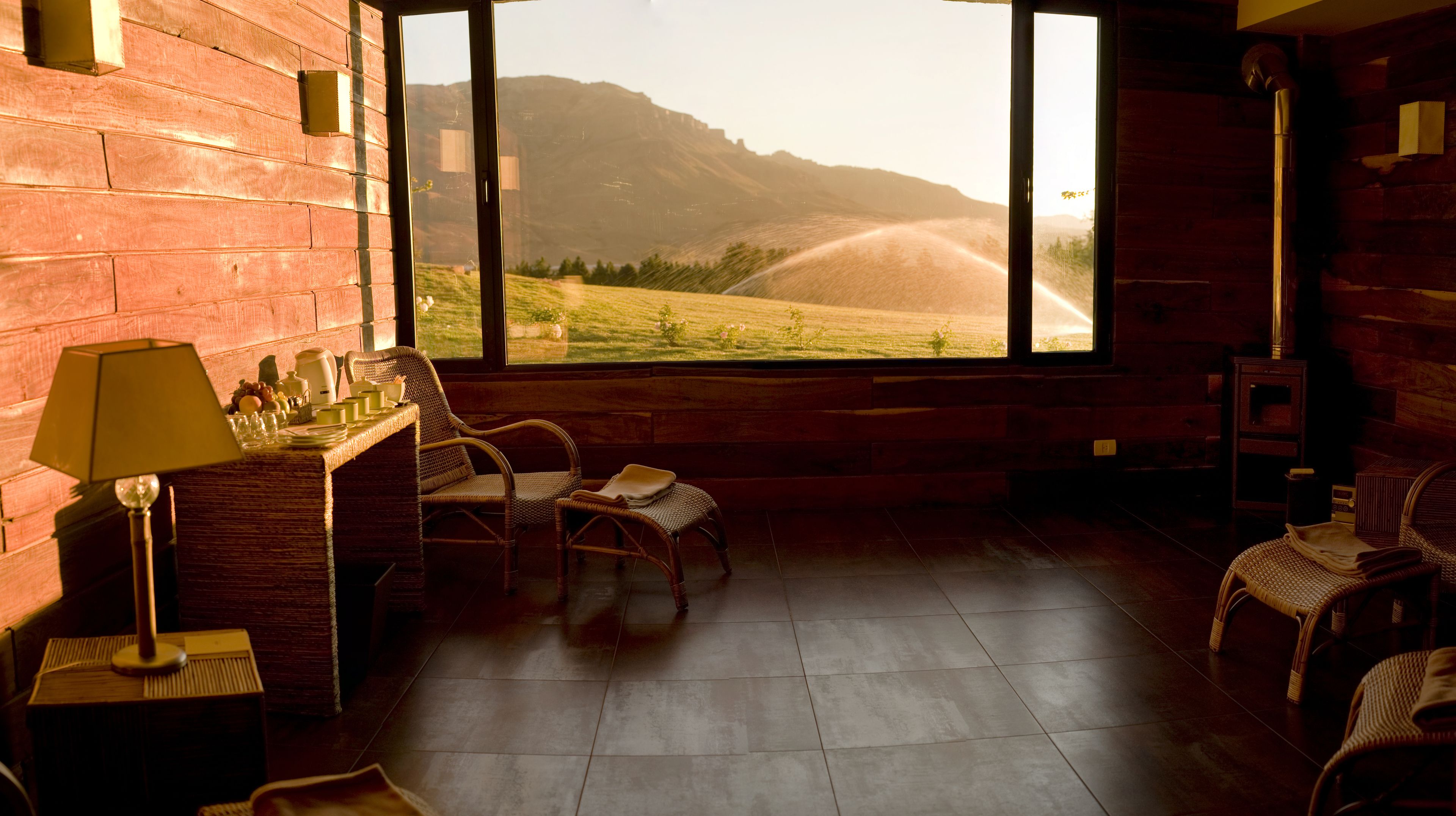 A room with a large window overlooking a scenic landscape, wicker furniture, and a wooden floor.