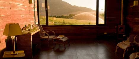 A room with a large window overlooking a scenic landscape, wicker furniture, and a wooden floor.
