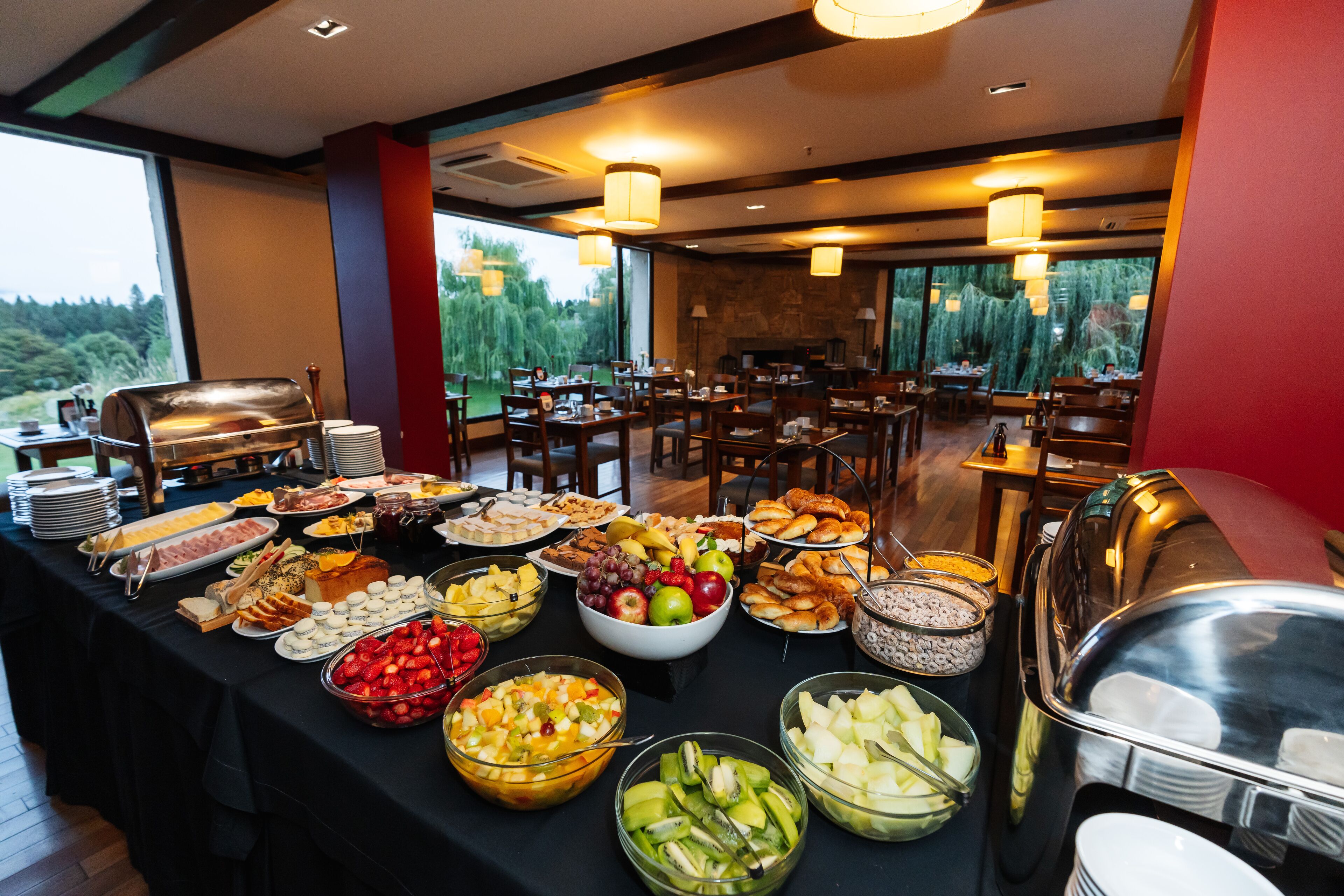 A buffet with various food items and a view of a forest through large windows.