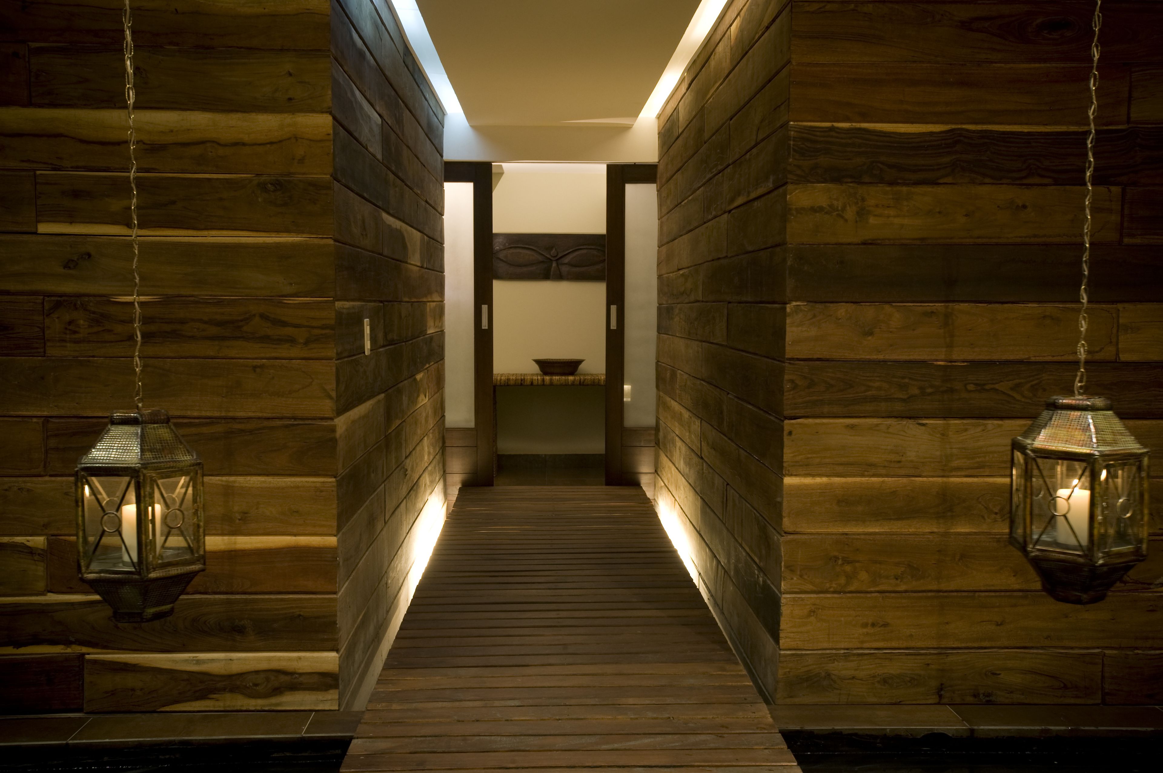 A wooden hallway with lanterns on either side, leading to a room with a bed and a small table.