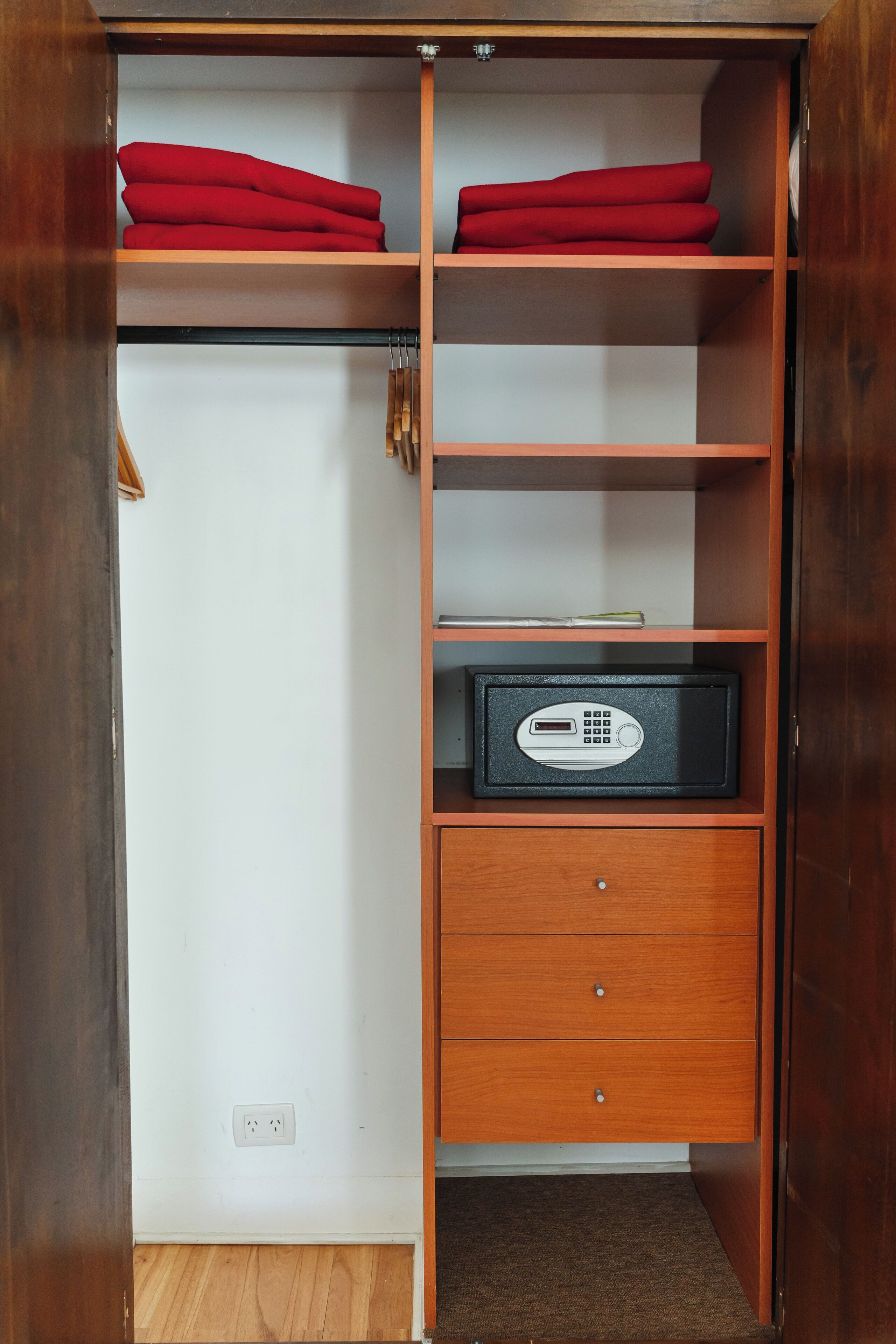 Un armario de madera con repisas, tela roja en la parte superior, una caja fuerte negra y un cajón.