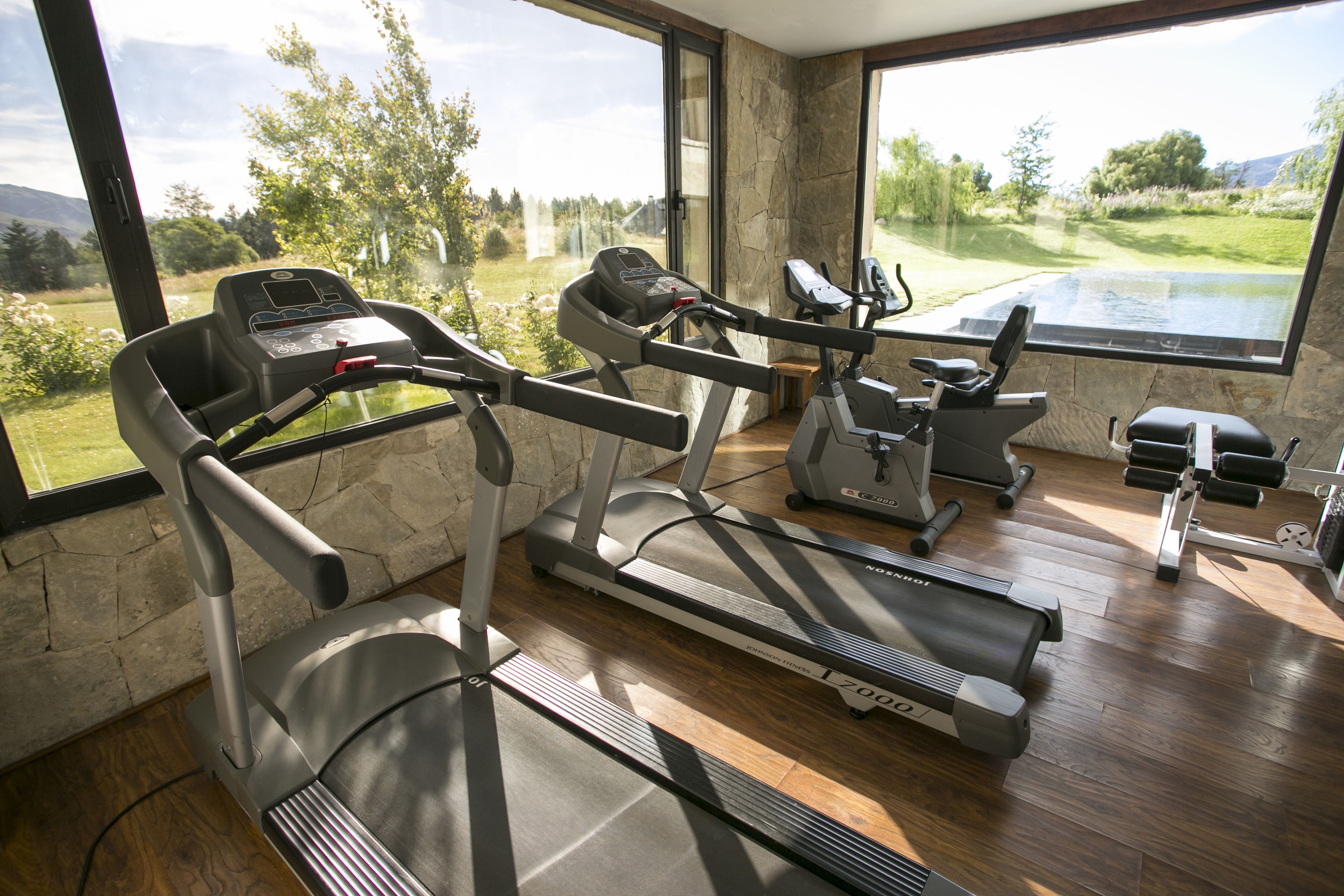 A home gym with treadmills, an elliptical, and a bench, featuring large windows with a view of a golf course.