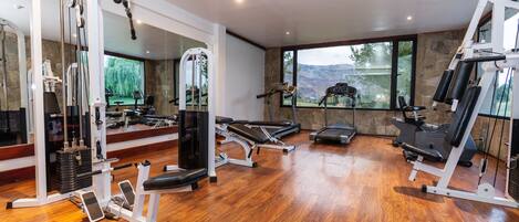 Un gimnasio espacioso con diversos equipos de ejercicio, amplias ventanas que ofrecen vistas al exterior y suelo de madera.