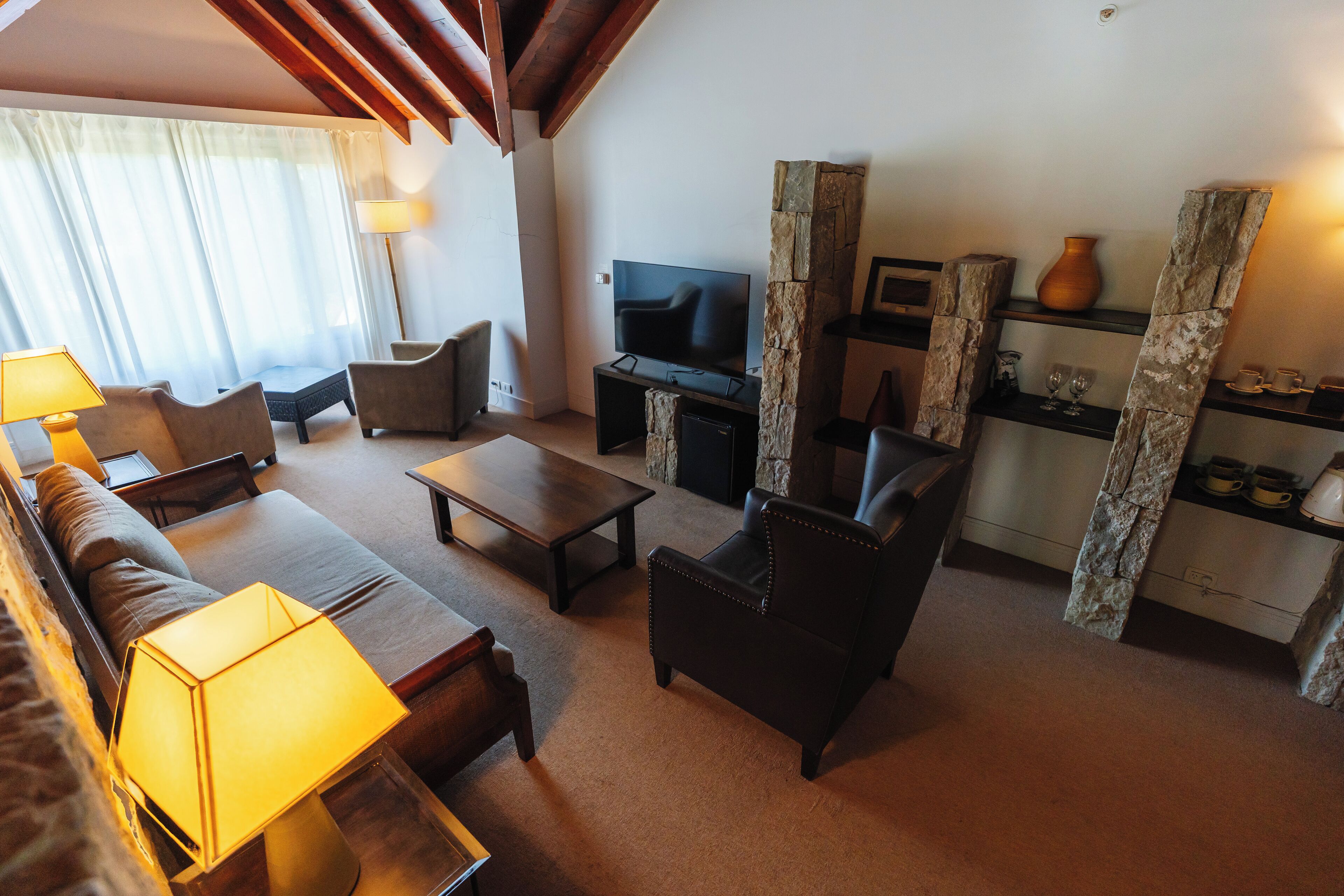 A living room with a sofa, armchairs, a coffee table, a TV, and a stone fireplace.